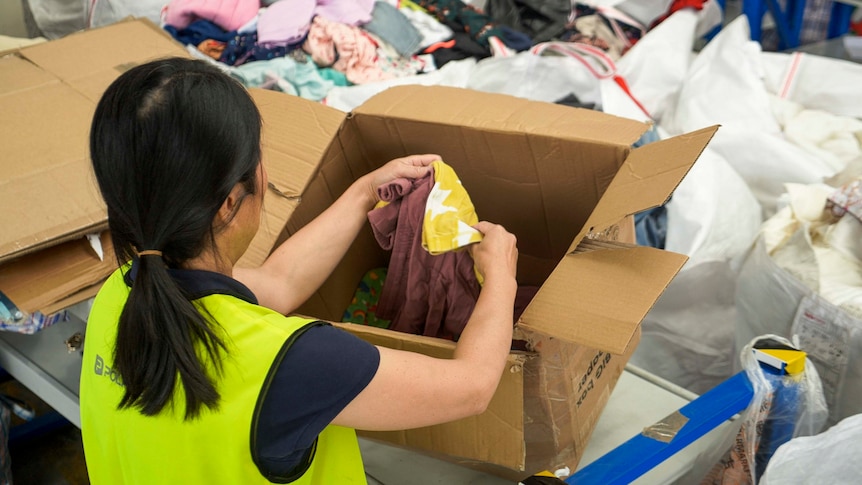 A woman in a flouro vest pulls out an item of clothing from a cardboard box