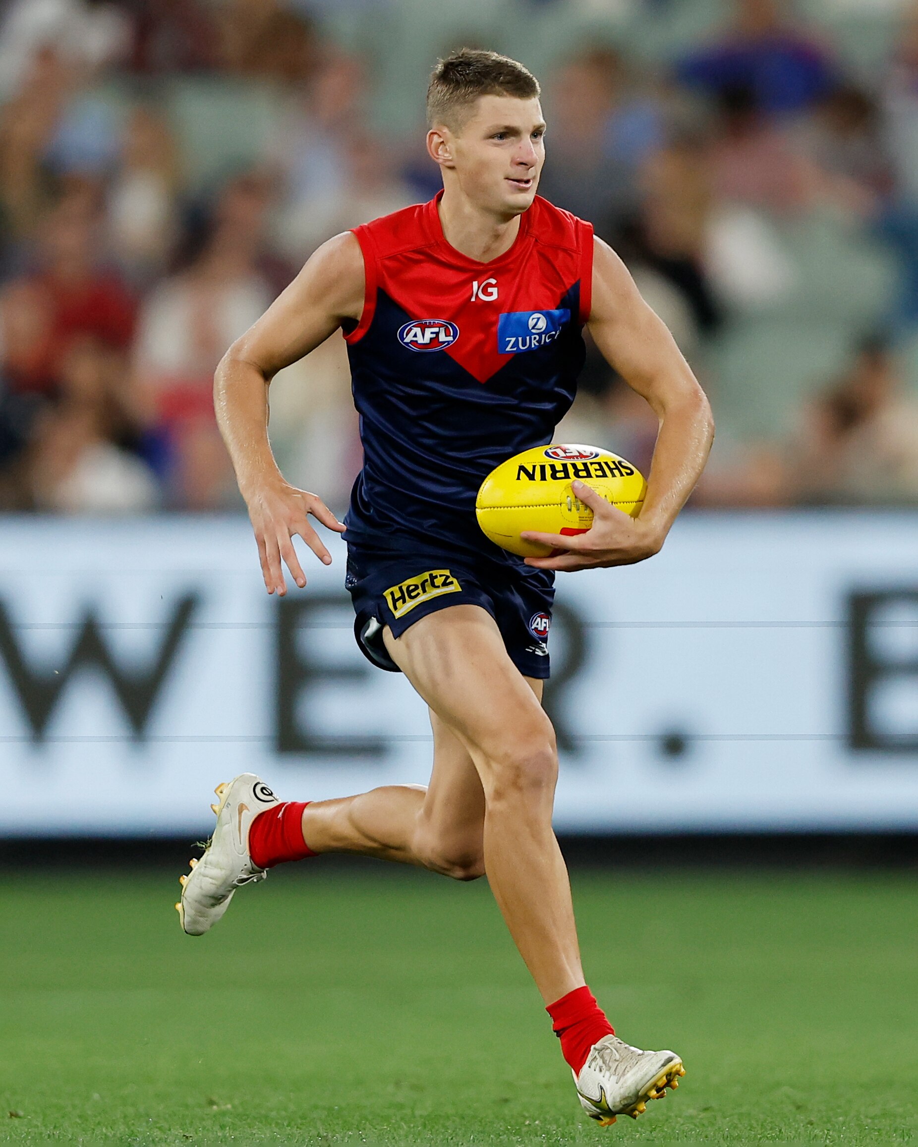 player in blue and red jumper running with afl ball on field