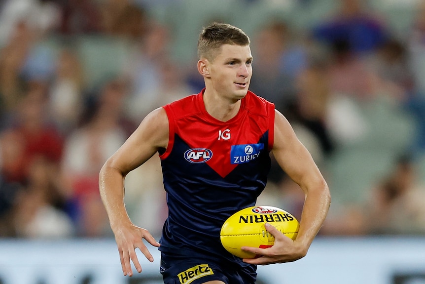 player in blue and red jumper running with afl ball on field 