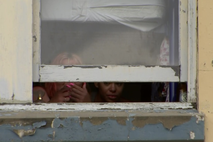 Two women looking out of a window, one is smoking.