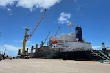A container ship at dock in a port with a crane over it.