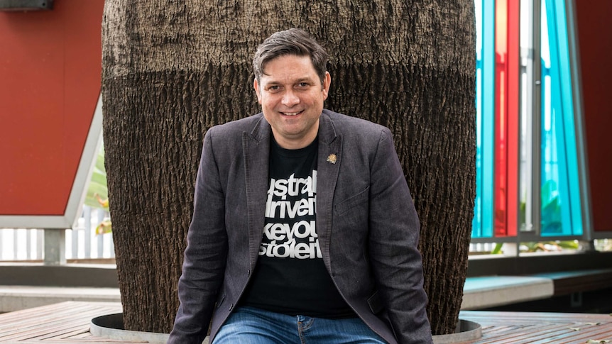 Colour photograph of Sydney Festival artistic director Wesley Enoch sitting in on a bench outside.