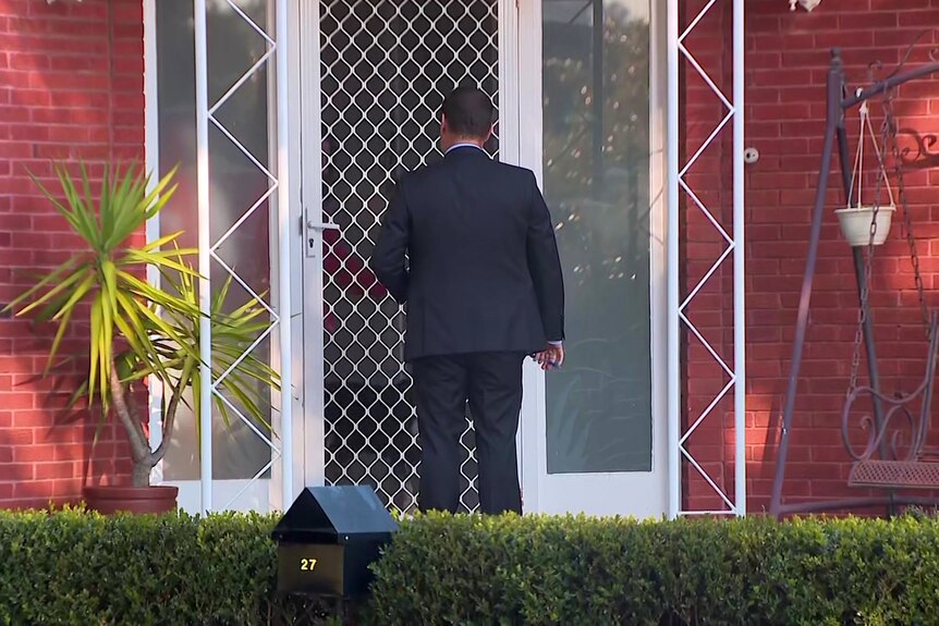 a detective stands outside a screen door after knocking waiting to speak to someone inside 