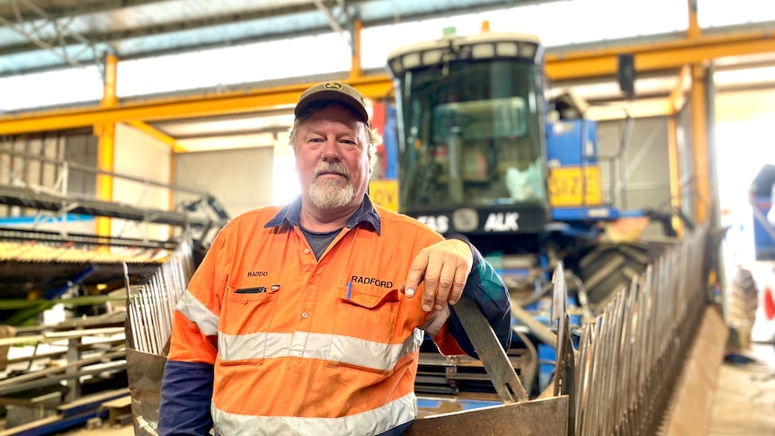 Man in high-vis leans on the front of a poppy harvester in a large workshop