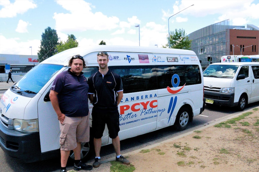 Two men stand outside a white van which has words 'PCYC' on it/