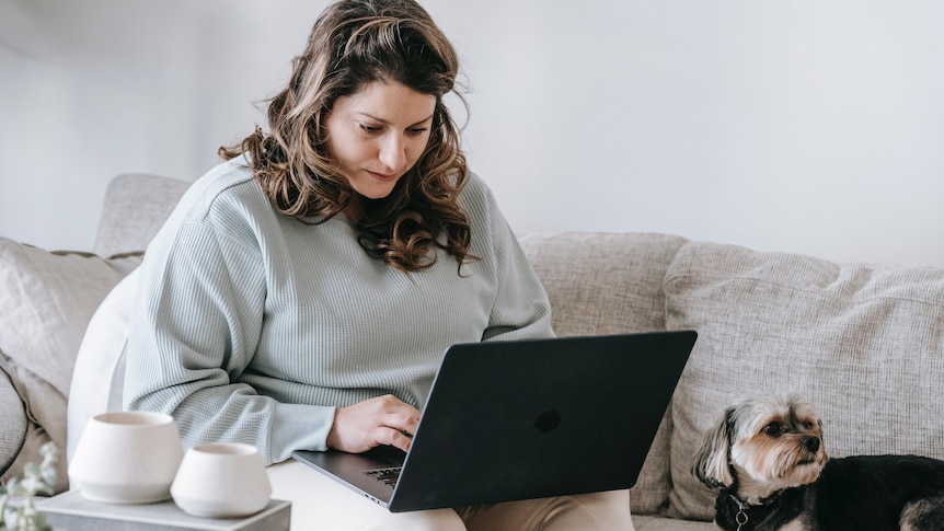 A woman sits on a couch and works on her laptop. 