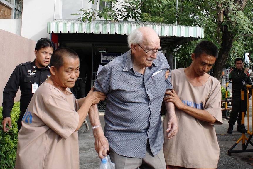 Detainees help Joseph Karl Kraus, a 90-year-old Australian man, as he leaves a court in Chiang Mai in Thailand.