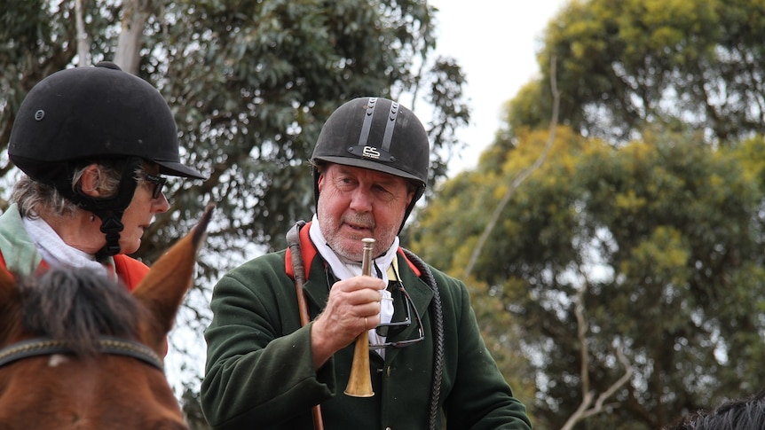 A man in a hard hat on horseback holding a small horn.