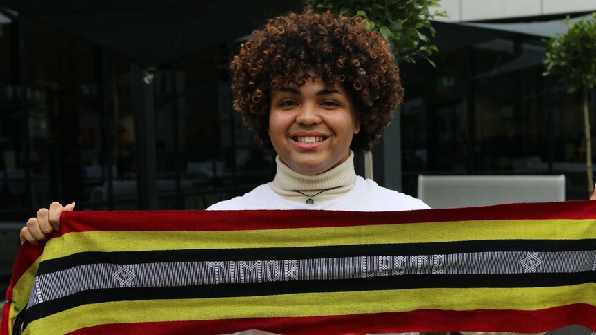 Samuel holds a scarf with the words Timor Leste.