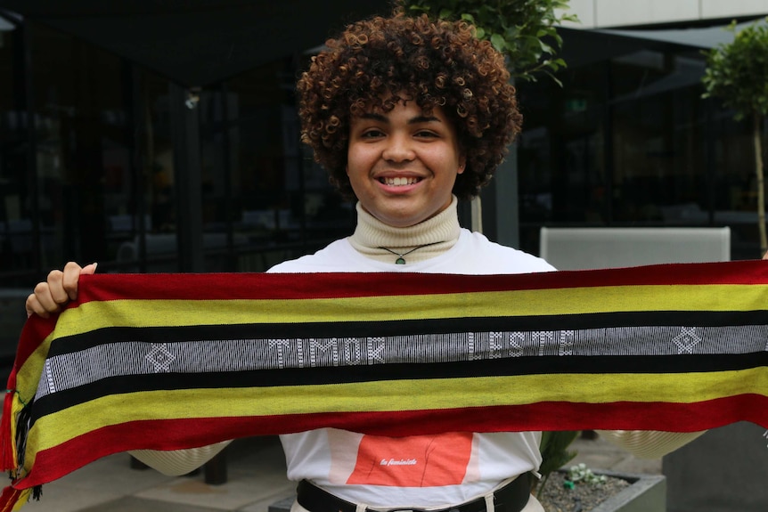 Samuel holds a scarf with the words Timor Leste.