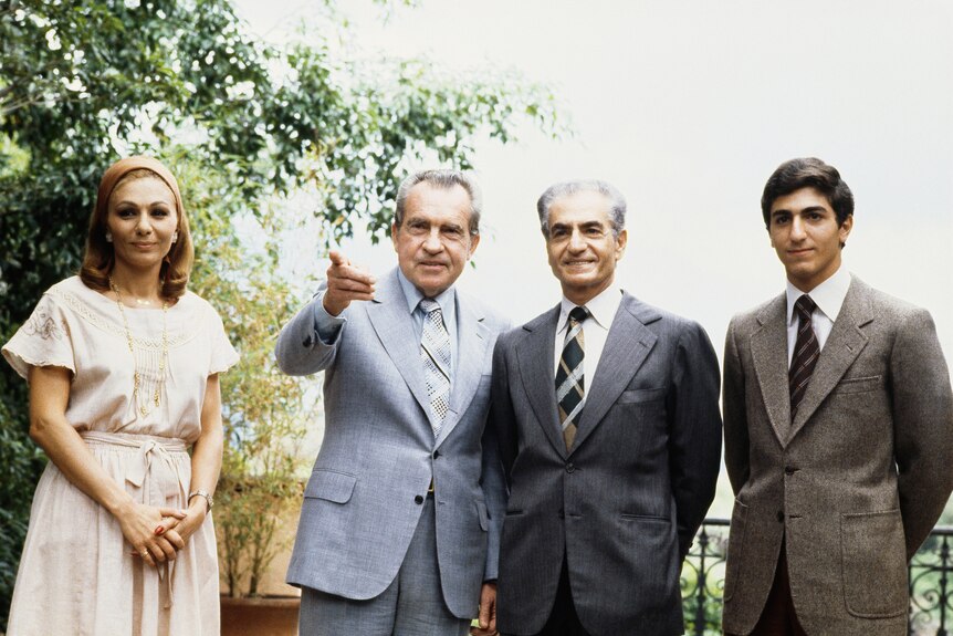 Four people standing on a balcony with trees beyond. Nixon is pointing at something off camera, the rest are looking at camera.