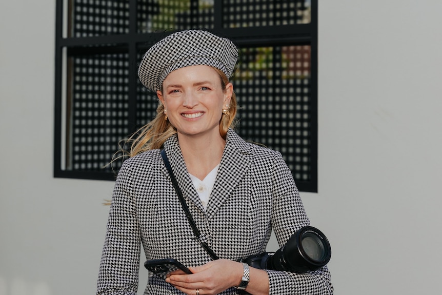 A young blonde woman smiling in a matching houndstooth beret and blazer. 