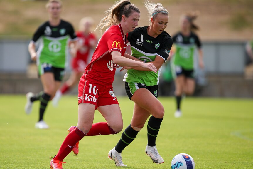 An Adelaide United A-League Women player is challenged by a Canberra United opponent.