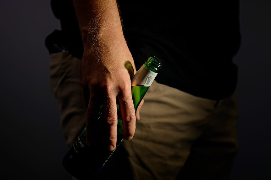 A man's hand holding a bottle of beer. 