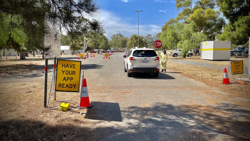 A yellow traffic sign reading 'have your app ready' next to a white SUV with someone in PPE talking to the driver