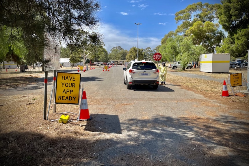 A yellow traffic sign reading 'have your app ready' next to a white SUV with someone in PPE talking to the driver