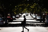 Silhouette of man crossing a street with harsh sunlight.