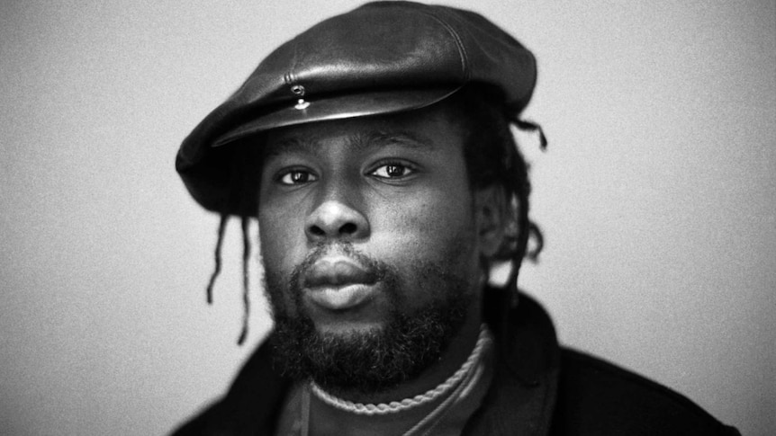 Black and white photo of Jamaican bassist and record producer Robbie Shakespeare. He wears a leather cap and dreadlocks