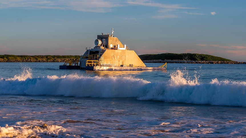 A concrete platform with a hole for a turbine in shallow waters at a beach.