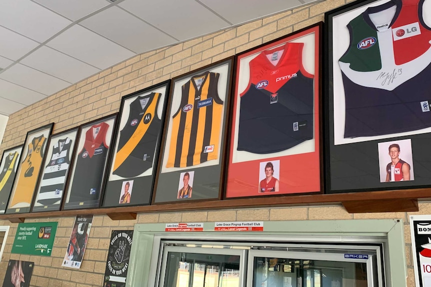 A row of AFL jumpers inside frames is hung high on a brick wall.