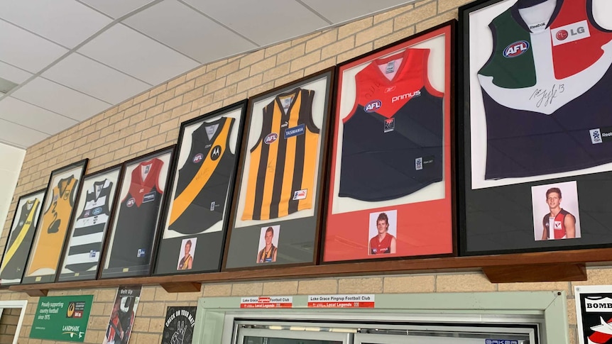 A row of AFL jumpers inside frames is hung high on a brick wall.