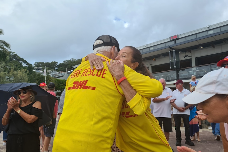 A man and woman in surf life saving uniforms hug