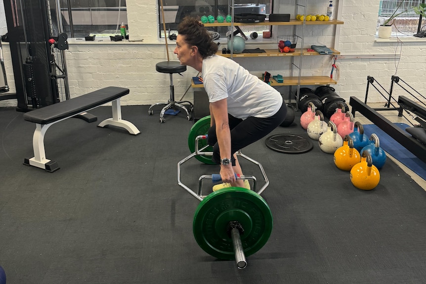 Virginia Trioli in workout gear squats to lift a barbell with weights on each end
