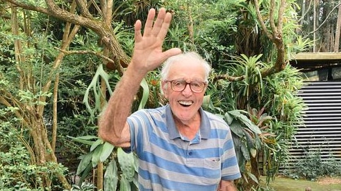 Elderly man waves at camera while holding letters