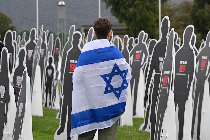 A protester with an Israeli flag walks past cutout cardboard effigies, representing Israeli hostages.