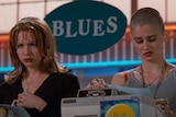Renee Zellweger and Robin Tunney stand behind a cash register looking unhappy in Empire Records