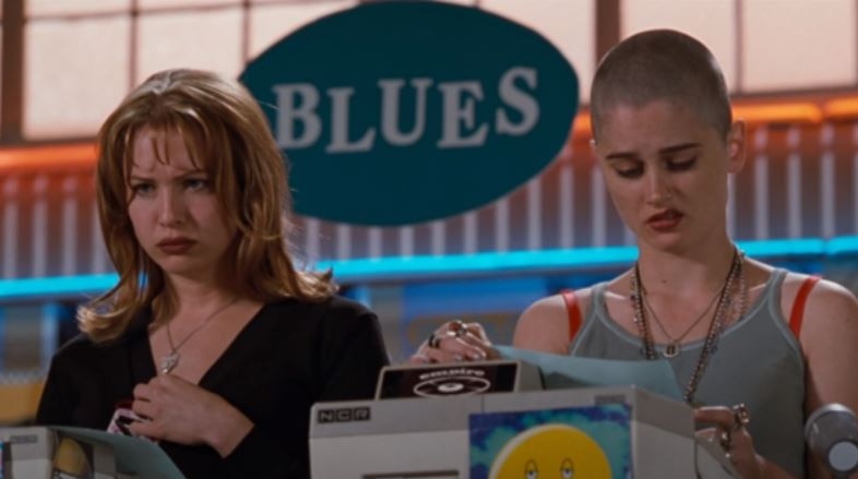 Renee Zellweger and Robin Tunney stand behind a cash register looking unhappy in Empire Records