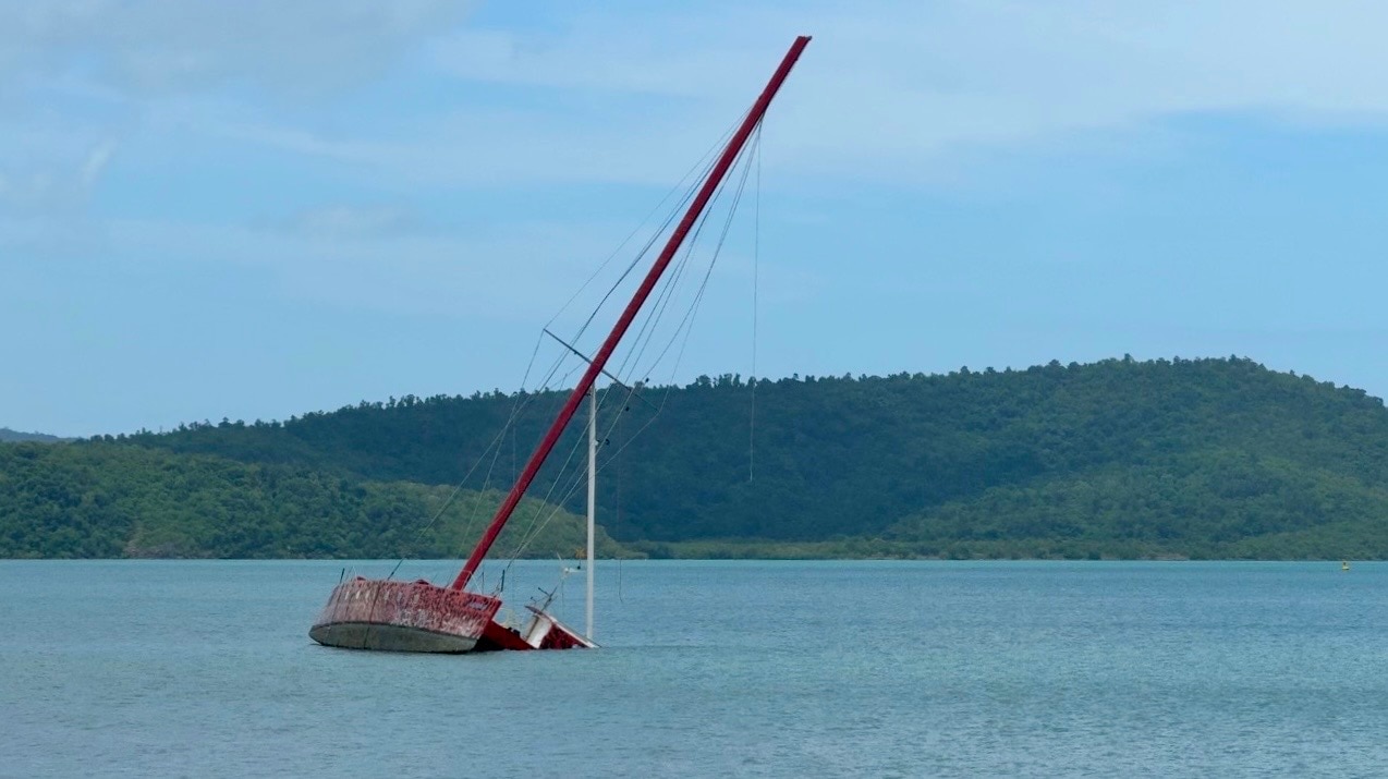 Un barco de tamaño mediano yace de costado en una zona poco profunda del mar frente a la playa de Cannonvale. 