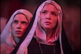 Two women in nun's habits are looking at something, their faces are bathed in red light