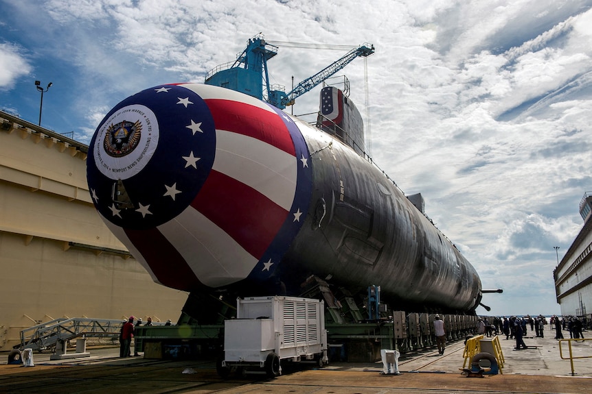 A submarine with a red, white and blue flag on the front sits on an empty patch of concrete