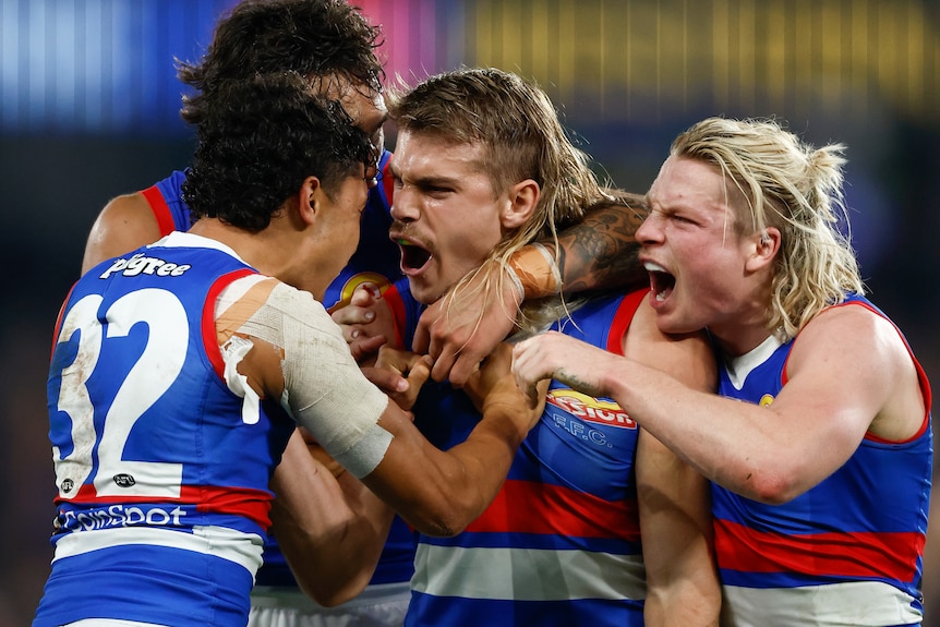Bailey Smith yells in delight while in a tight hug with a number of Bulldogs teammates