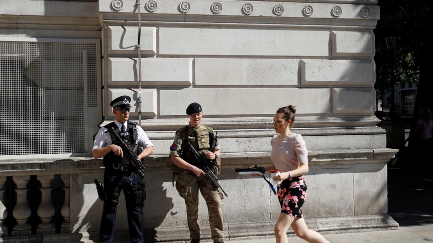 A woman rushes past a soldier and an armed police officer on duty on Whitehall in London, Britain.