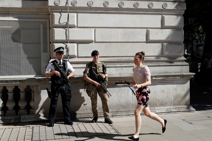 A woman rushes past a soldier and an armed police officer on duty on Whitehall in London, Britain.