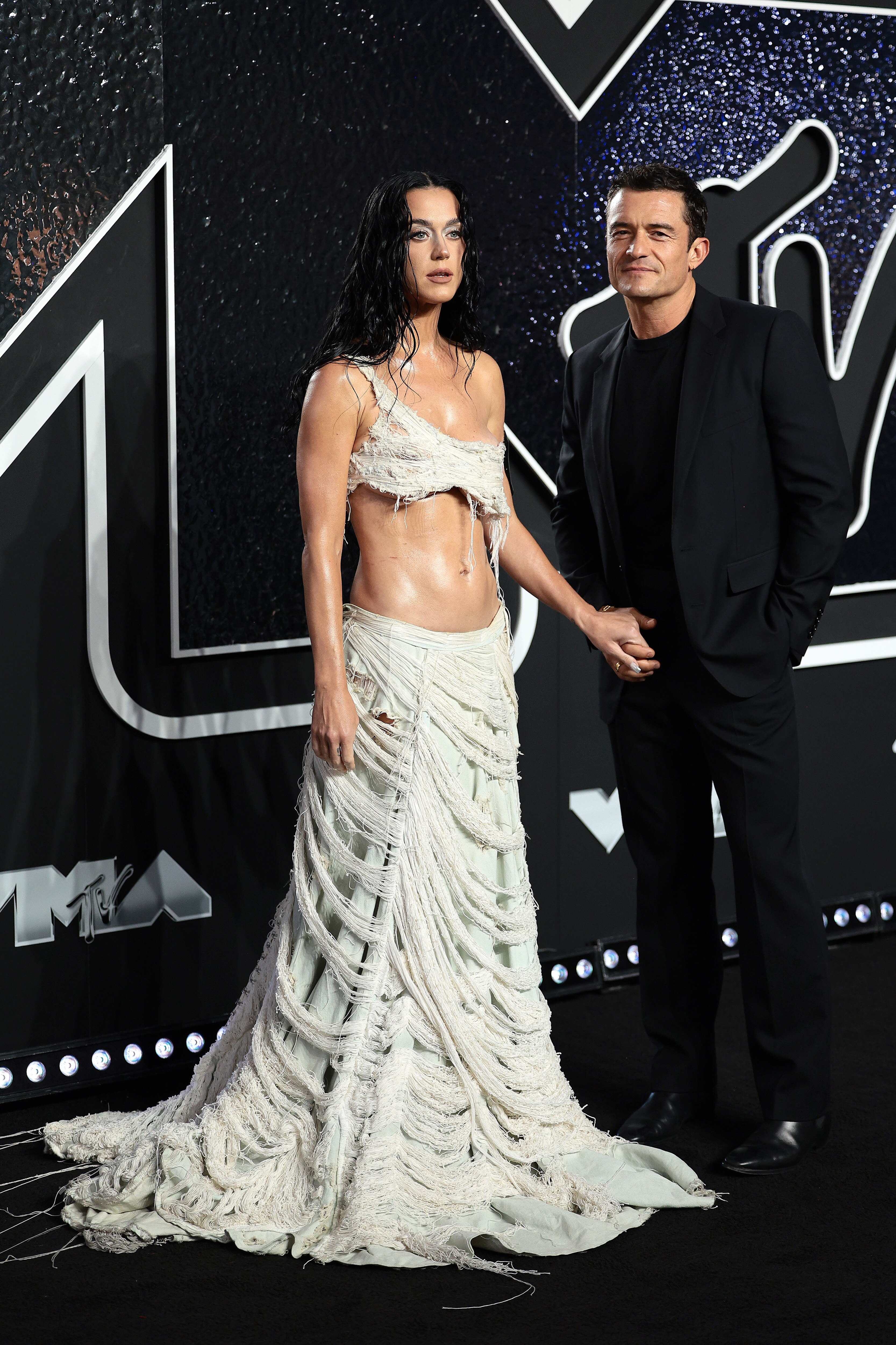 Katy Perry and Orlando on the VMAs red carpet. Katy is wearing a white top and skirt while Orlando is wearing a black suit