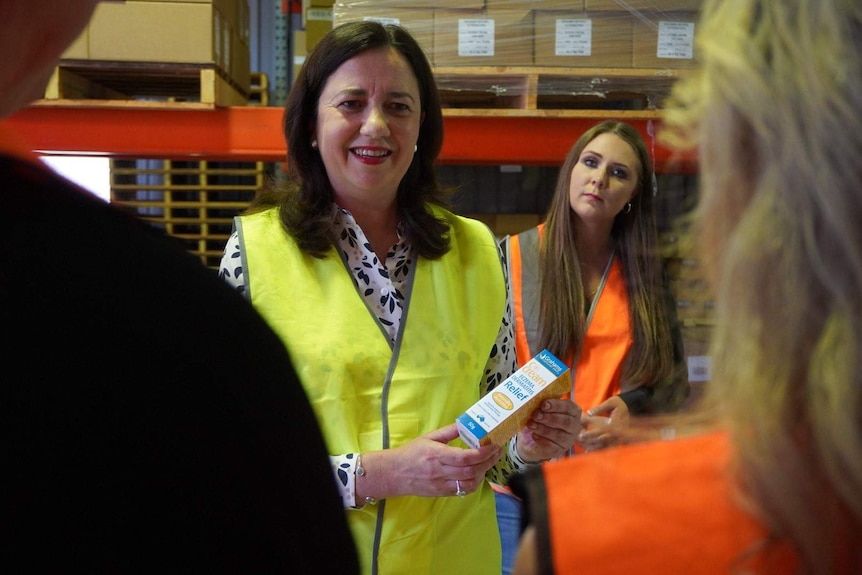 Woman in high-vis vest speaks to workers while holding a bottle of skin cream