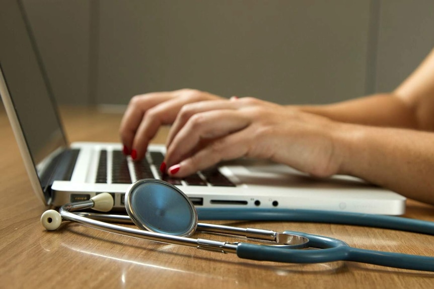 Hands on a laptop next to a stethoscope.