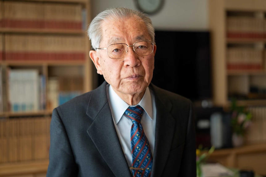 An older man in a suit and glasses looking sombre