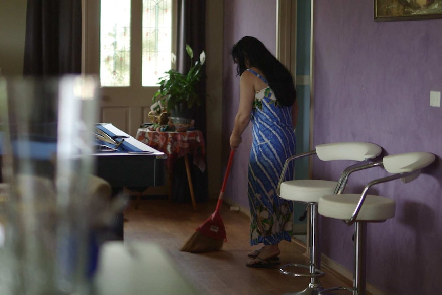 A woman sweeps the floor of a house