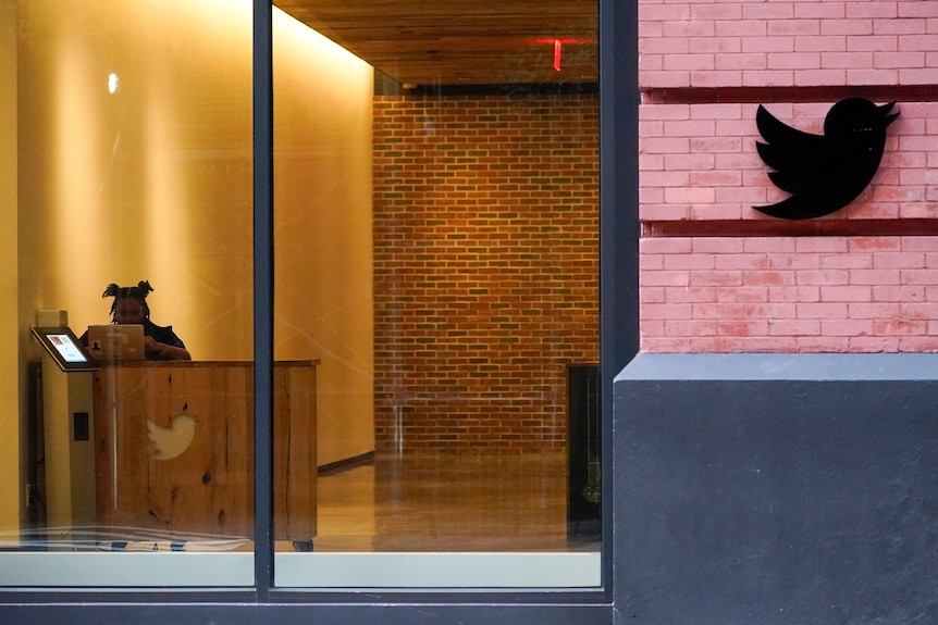 a woman behind a mac book seen from behind glass doors in the twitter lobby