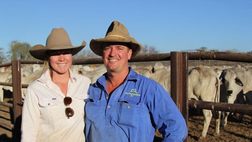 A smiling farming couple smile near some cattle