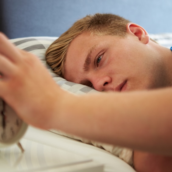 A sleepy teen with his hand on an alarm clock