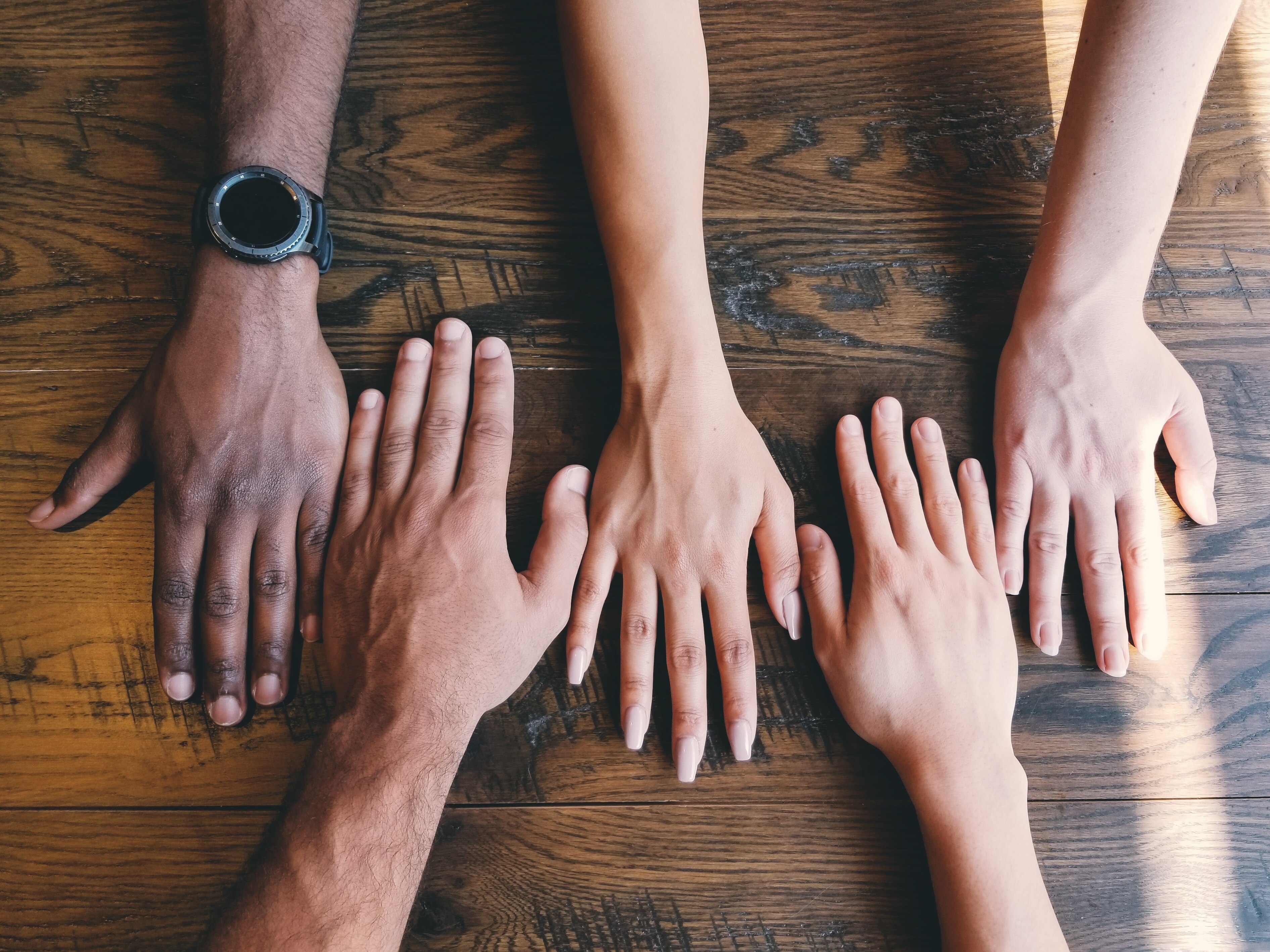 Five hands on a table belonging to people of different skin tones