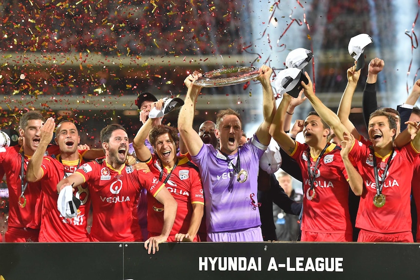 Adelaide United players celebrate with the A-League trophy