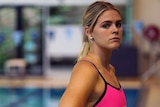 A young blonde woman stands beside a pool wearing a neon pink swimsuit