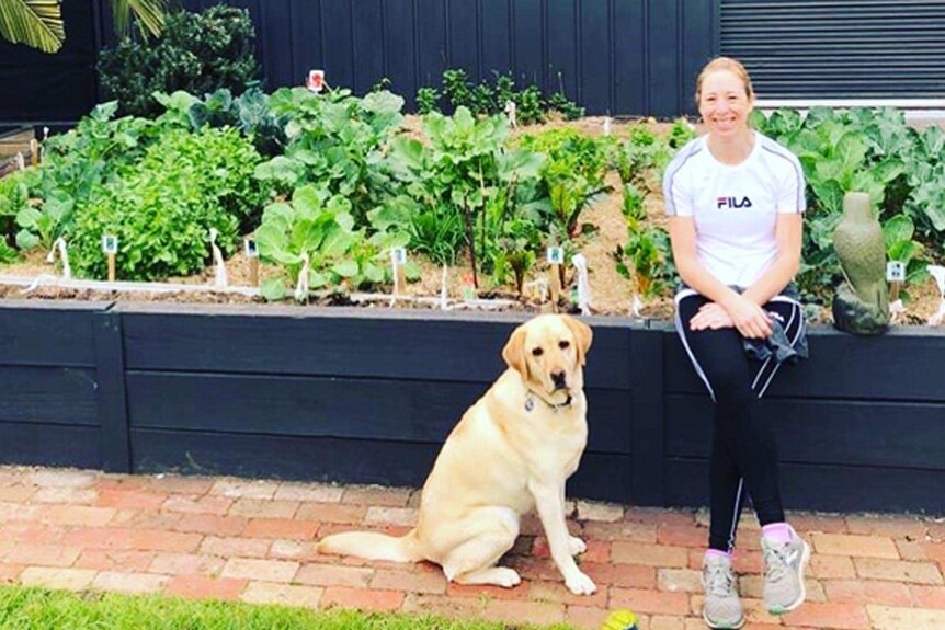 Rebecca Purvis sitting with her dog in front of her vegetable garden