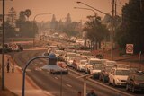 A long line of cars not moving on a winding road with bushfire smoke in the air.